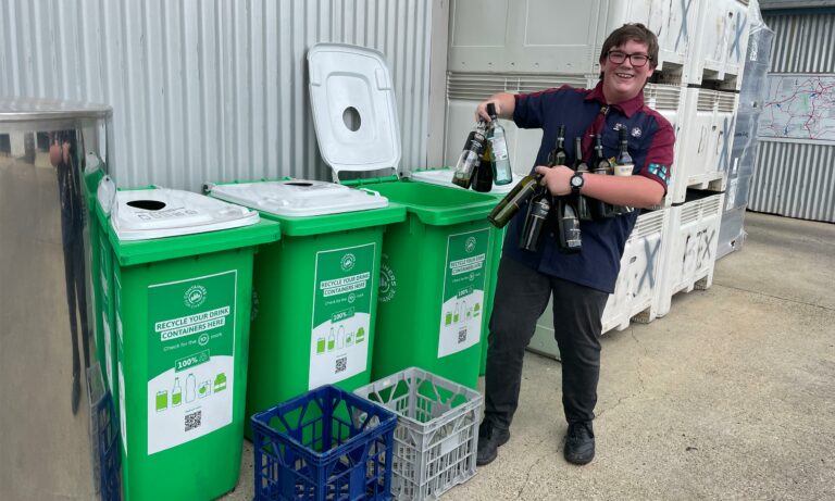 Young man recycling wine bottles mat green bins