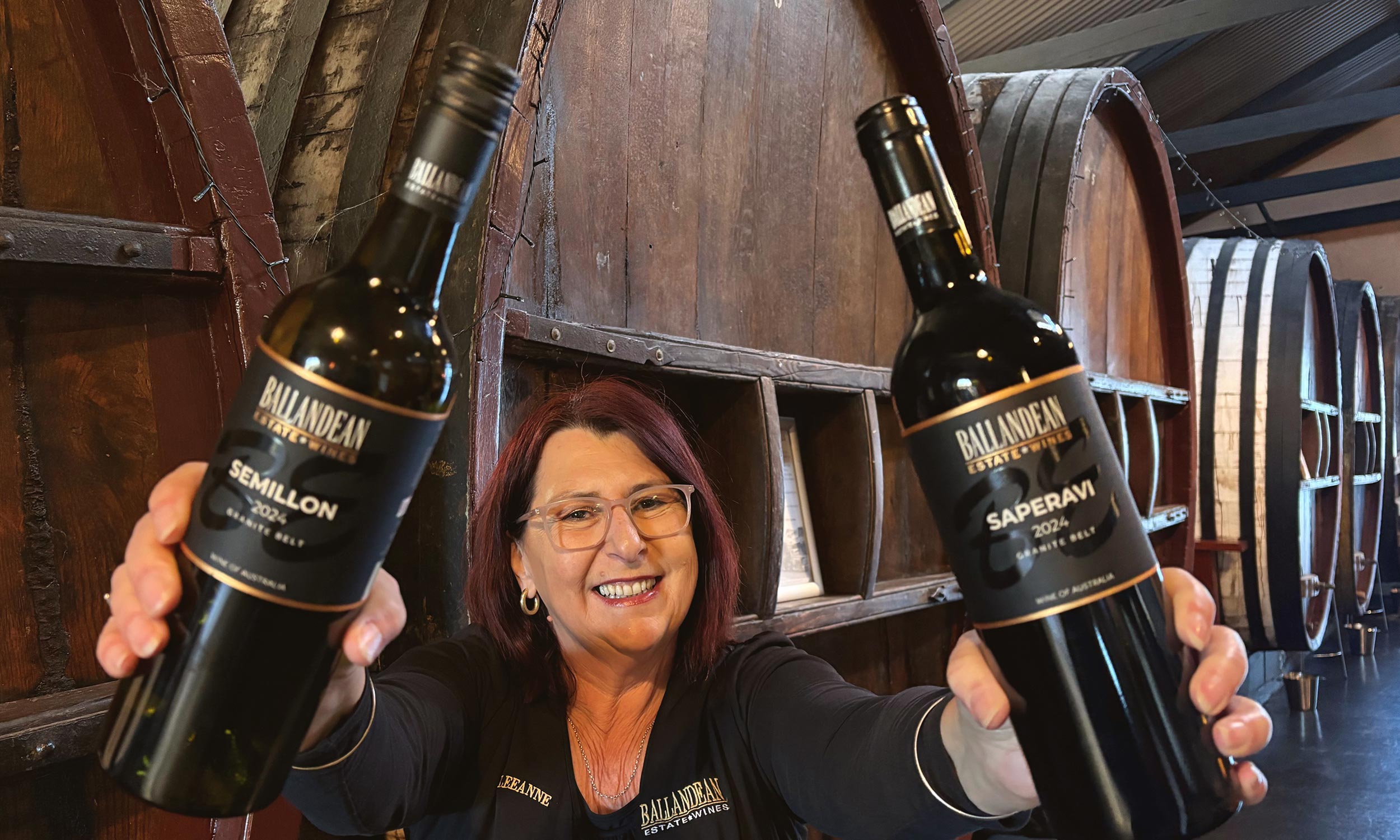 Brunette woman holds two wine bottles in the air with a joyous expression on her face