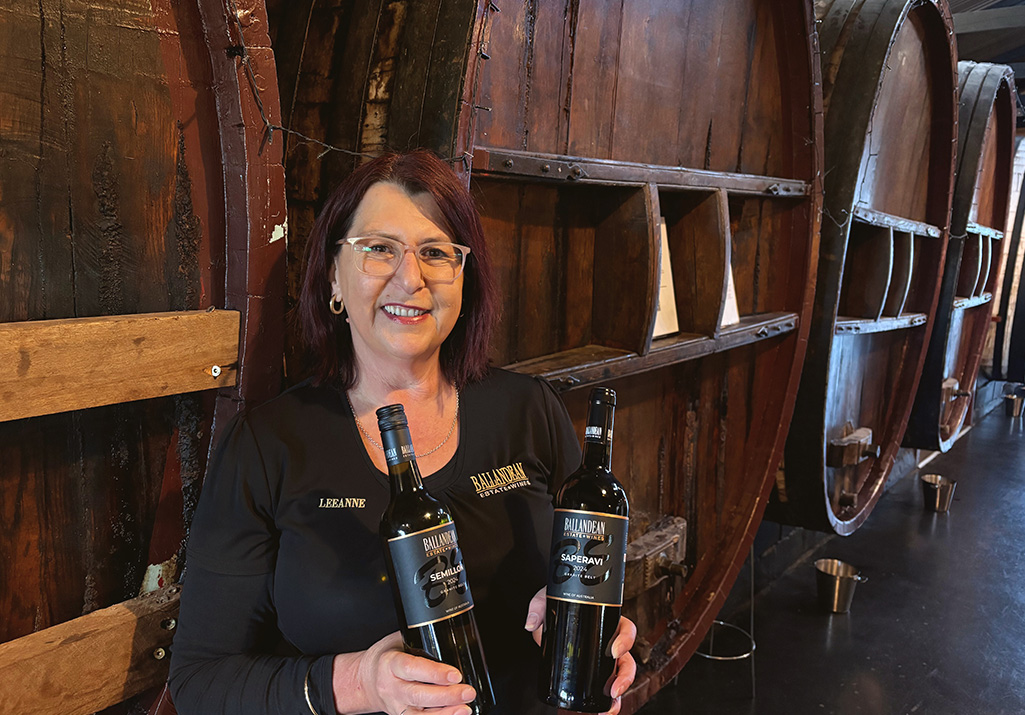 Woman holding two bottles of wine in front of port barrels